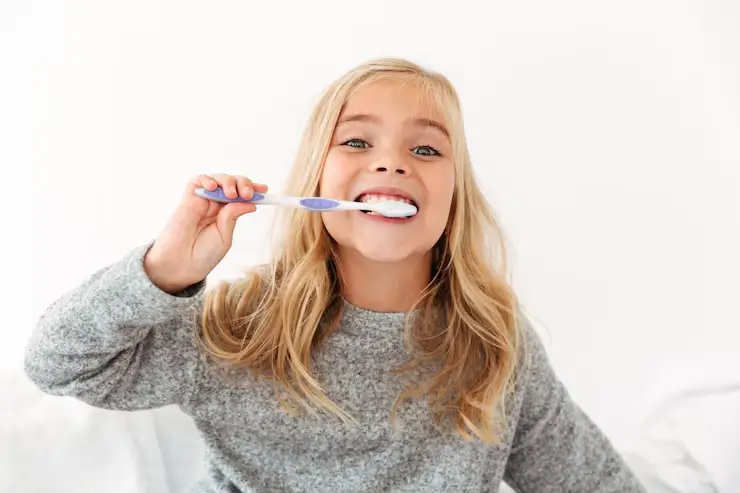 Cheerful young girl with blonde hair brushing her teeth, showing daily oral care habits taught at ZPD Dental Clinic