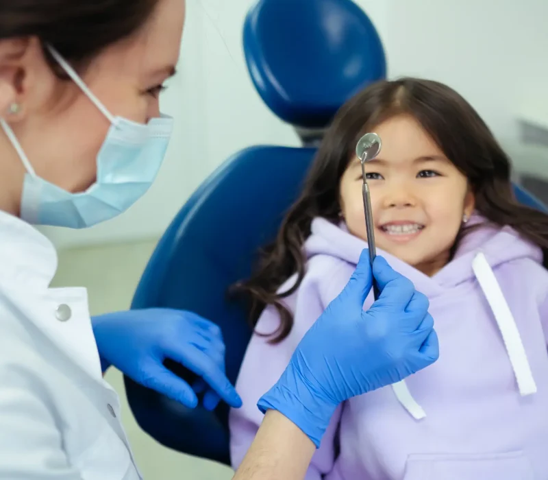 Young girl smiling confidently at dental mirror during check-up at ZPD Dental Clinic